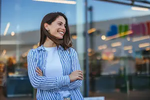 A smiling woman with arms crossed standing outside a store with a colorful sign