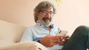 A man with a beard is sitting on a couch and holding a cell phone.
