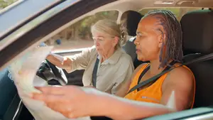 Two women inside a car, one is holding a map and the other is driving