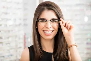 Woman adjusting her glasses while smiling in a blurry background