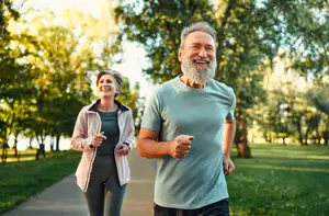 An older man and woman are jogging in a park during the daytime.