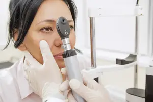 A woman is examining her eye with a medical device, possibly a doctor or an optometrist.