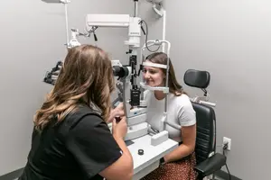 A woman is having her eyes checked by another woman in a medical room.