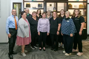A group of people standing in an office space wearing various clothing and footwear, some smiling and looking at the camera.
