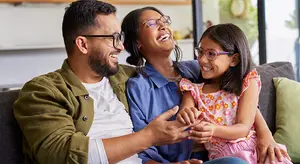 Father and two daughters laughing and smiling while sitting on a couch.