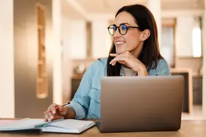 woman smiling while sitting at a desk with a laptop and book