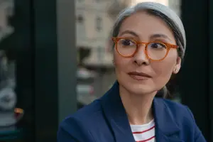 Gray-haired woman wearing blue jacket and orange glasses posing for a photo