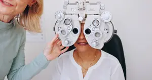An optometrist assisting a woman in testing her vision using an eye chart.
