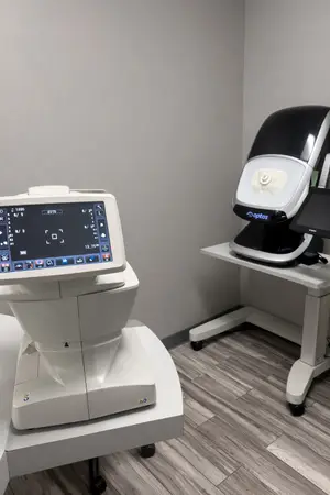 Two medical equipment devices, one with a monitor and the other with a screen, are on top of a white table in a room with a wooden floor and a gray wall.
