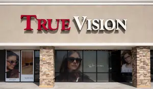 A store exterior with a sign that reads True Vision and displays glasses on the windows.