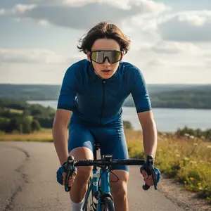 A cyclist in blue riding gear, wearing sunglasses, rides down a scenic road with a lake in the background.