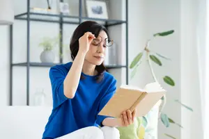 A woman wearing glasses and reading a book on a couch