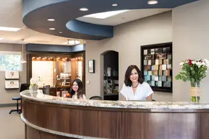 Two women stand behind a marble counter in a medical office, smiling and posing for a photo