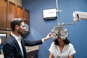 A man with glasses adjusts a woman's eye chart in an eye doctor's office.
