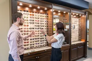 A man and a woman standing in front of a cabinet filled with sunglasses in a shop