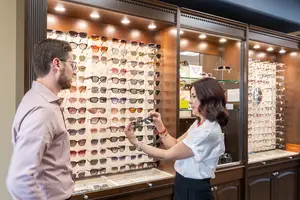A woman wearing a watch is showing sunglasses to a man in a store with wooden cabinets and lights
