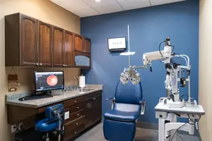 An eye examination room with a monitor, sink, cabinets, and medical equipment.