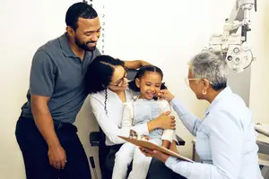 A young girl with her family is having her eyes checked by a doctor in a clinic.