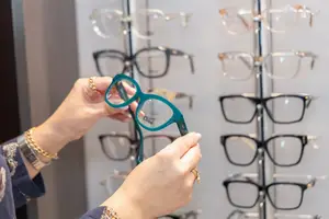 A woman is examining glasses in a retail setting, surrounded by various frames on display.