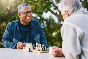 Two elderly men sitting at a table, smiling, and playing chess.