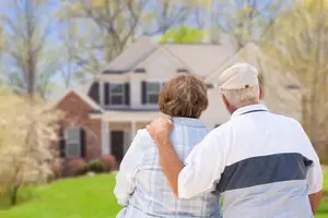 An elderly couple standing in front of their house in a garden area