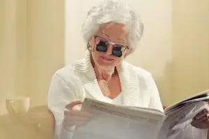 An elderly woman wearing glasses and reading a newspaper