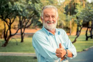Portrait of an elderly man standing in a park with a smile and thumbs up gesture