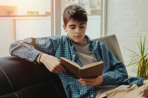 A boy sitting on a couch reading a book