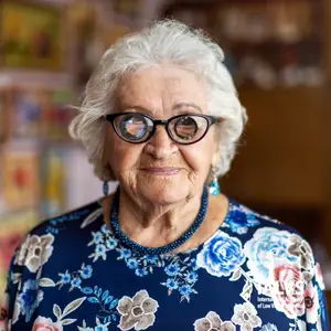 Portrait of an elderly woman with glasses and a floral dress smiling for the camera